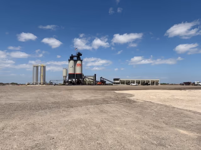 Wide view of an industrial plant with storage silos under a partly cloudy blue sky.